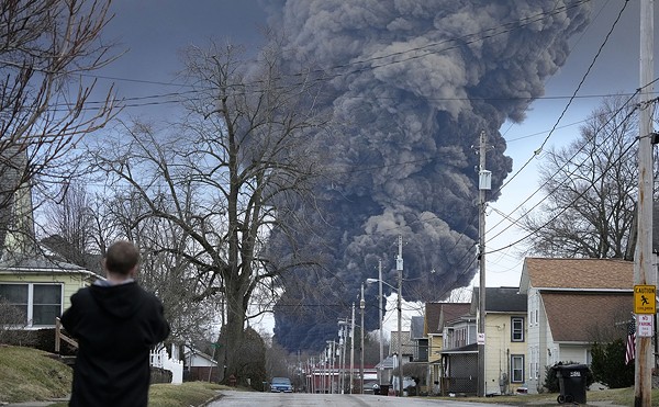 A man takes photos as a black plume rises over East Palestine, Ohio, as a result of a controlled detonation of a portion of the derailed Norfolk Southern train, Feb. 6, 2023. After toxic chemicals were released into the air from a wrecked train in Ohio, evacuated residents remain in the dark about what toxic substances are lingering in their vacated neighborhoods while they await approval to return home. (AP Photo/Gene J. Puskar, File)