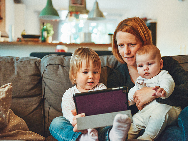 A mother holding two small children and an iPad