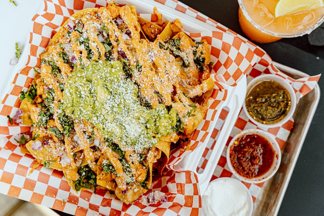 Guti Nachos with pollo asado: corn chips topped with refried beans, guacamole, mozzarella, cilantro, onion and cotija cheese, served with sour cream, roja and verde salsas