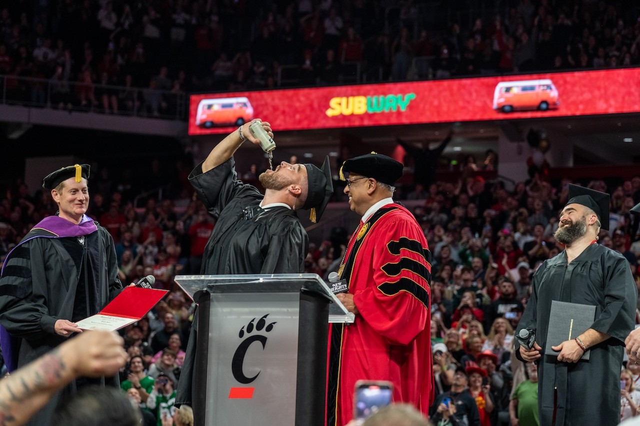 Travis Kelce chugging beer during his surprise graduation ceremony at the New Heights podcast live show at Fifth Third Arena | April 11, 2024