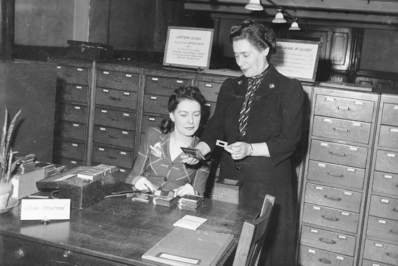 Alice Plaut (standing), who worked there, chatting with another staff member about glass "lantern" slides used in the stereopticon
Photo: Courtesy of The Public Library of Cincinnati and Hamilton County Digital Archives