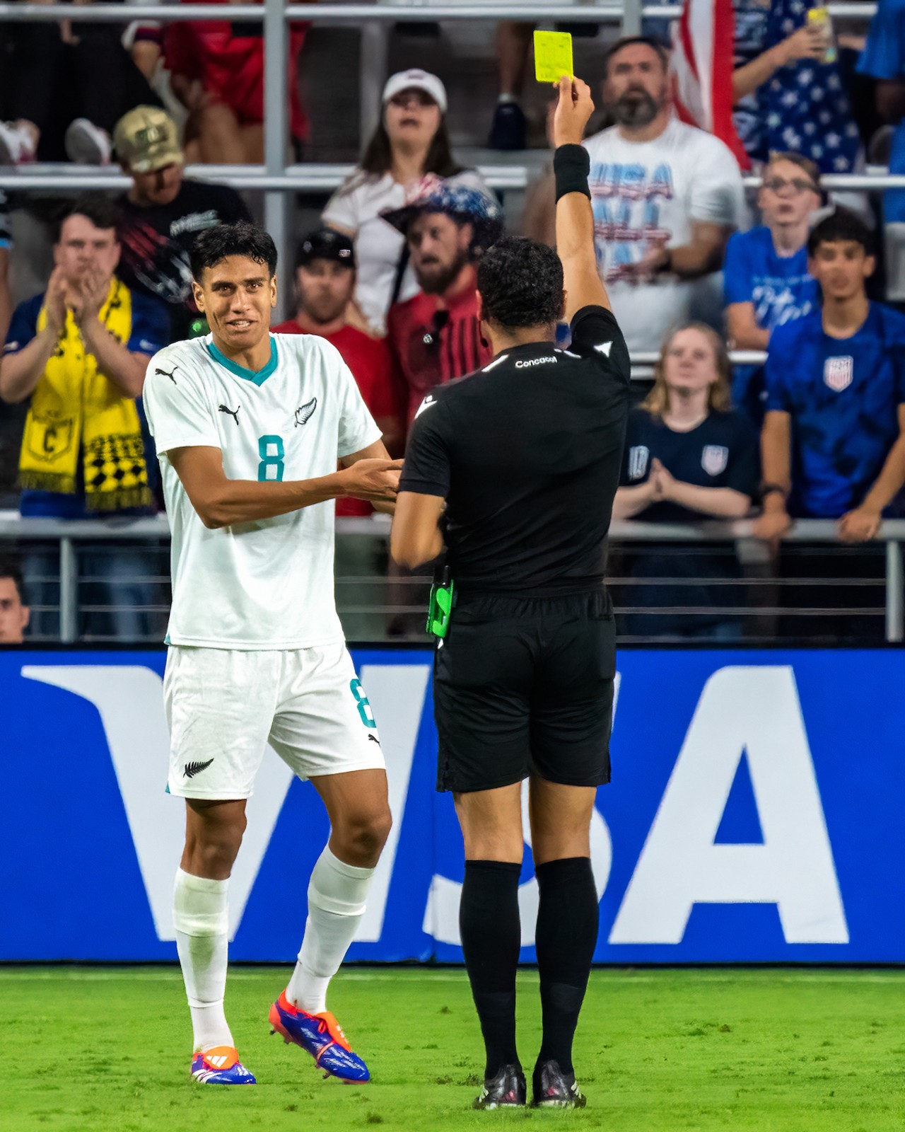 Referee Selvin Antonio Brown Chavarria issues yellow card to New Zealand player.