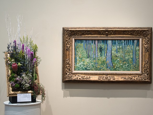 A floral display juxtaposed with Vincent van Gogh's "Undergrowth with Two Figures" during 2019's Art in Bloom.