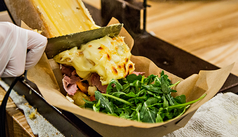 Raclette cheese being scraped onto a pile of veggies and ham and potatoes - Photo: Hailey Bollinger