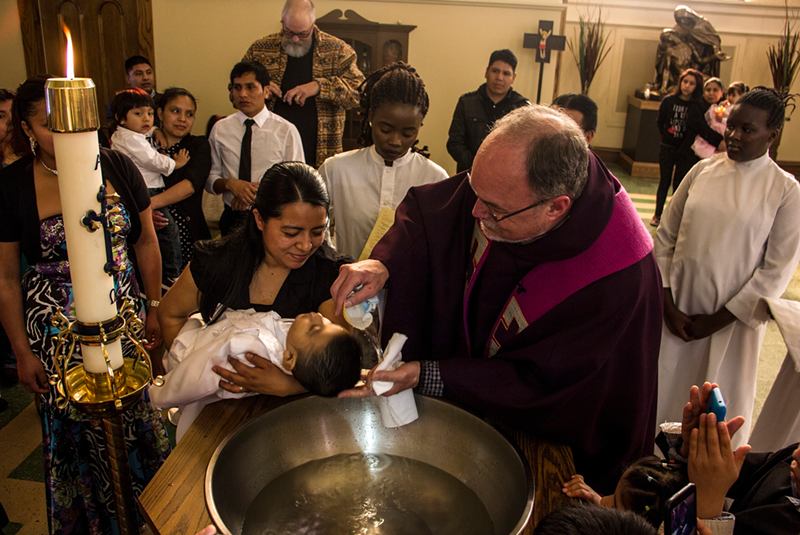 Father Jim Schutte baptizes the child of Guatemalan immigrants at St. Leo the Great Catholic Church in Cincinnati as congregants who are refugees from Burundi look on. - Photo: Nick Swartsell