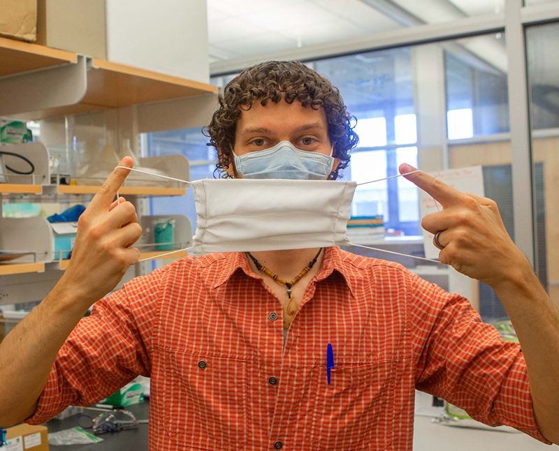 UC postdoctoral researcher Adam Parlin holds up a silk mask in a biology lab. - Photo: Joseph Fuqua II/UC Creative