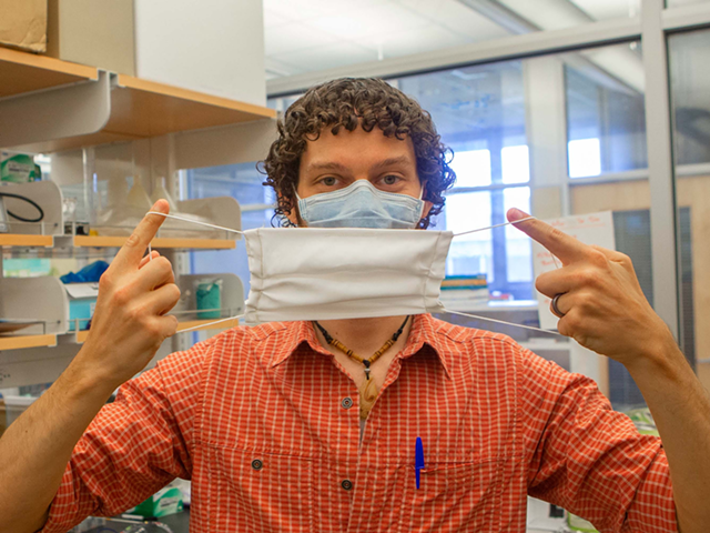UC postdoctoral researcher Adam Parlin holds up a silk mask in a biology lab.